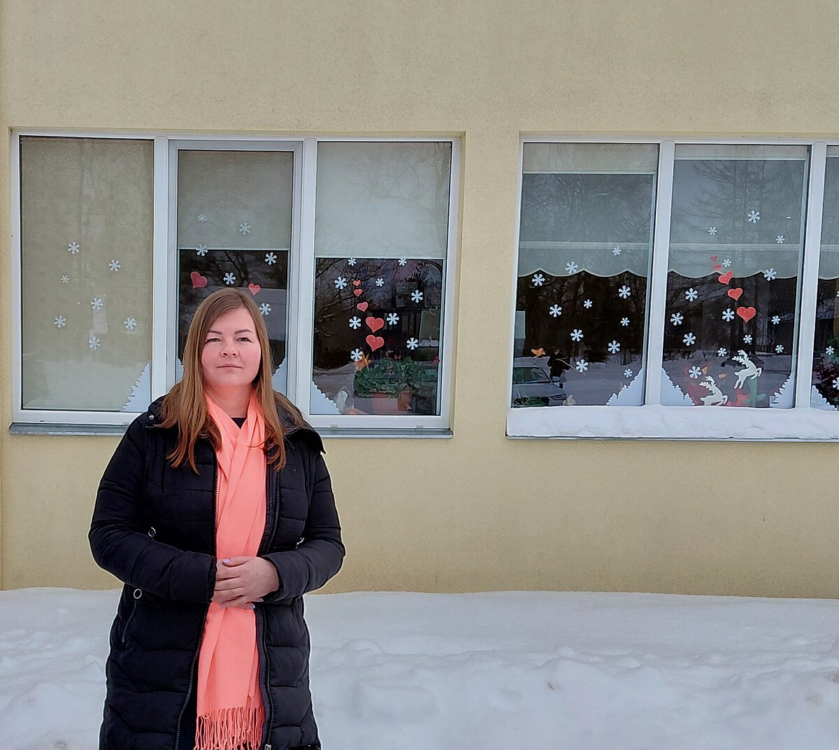 LU Madonas filiāles 2026. gada ziemas absolvente Evita Šuļja: "Šī ir vieta, kur aug ne tikai bērni, bet arī es. Katrs bērna smaids un apskāviens atgādina, ka es esmu daļa no kaut kā lielāka par ikdienas pienākumiem." Foto no personīgā arhīva LU Madonas filiāles 2026. gada ziemas absolvente Evita Šuļja ziemā ārā pie darbavietas izrotātajiem logiem